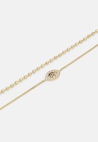 Bracelet en perles dorées avec un charme en forme d'œil détaillé, comprenant un petit centre noir et des strass clairs tout autour, texture lisse.