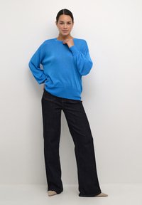 Maglione azzurro a maglia con una vestibilità rilassata e polsini a coste, abbinato a jeans neri a gamba larga. L'outfit presenta una texture liscia e dettagli minimi.