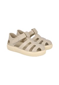 Sandalias de goma beige con un diseño abierto, que presentan correas anchas, detalles recortados y una suela texturizada para mejor agarre. Cierre de velcro.