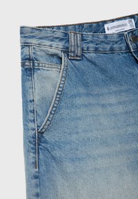 Jean en denim bleu clair présentant un design classique à cinq poches, une fermeture à bouton et un léger dégradé sur le tissu.