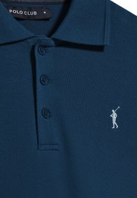Camisa polo en color navy con un tejido texturizado, tapeta de tres botones y un pequeño logotipo bordado en blanco en el lado izquierdo del pecho.