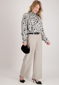 Lichtgrijze blouse met zwarte polkadots, gerimpelde halslijn en omgeslagen mouwen, gecombineerd met beige brede pantalons en een zwarte bonten clutch.