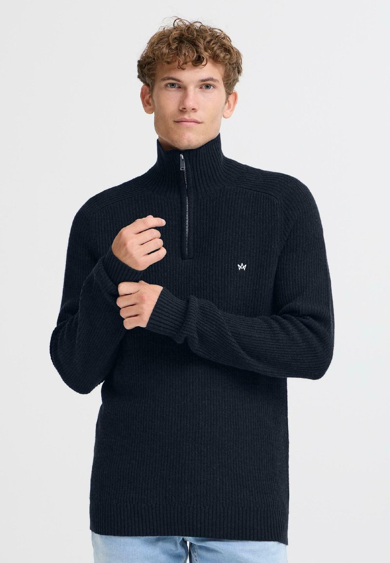 Maglione nero a costine con zip e colletto alto, dotato di un piccolo logo sul petto, maniche lunghe e vestibilità comoda.