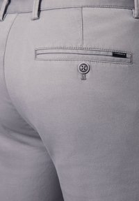 Szare spodnie wykonane z fakturowanej tkaniny, z tylną kieszenią na guzik oraz małą metką marki wszytą na tkaninie.