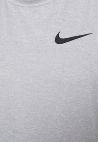 Camiseta deportiva gris con tejido texturizado, que presenta un logo de la marca Nike en color negro en el frente. Cuello redondo sencillo.