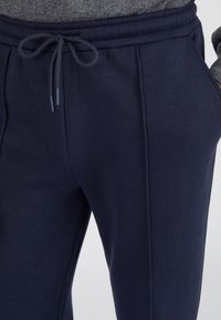 Pantalones deportivos azul marino con cintura elástica y cordón de ajuste, que presentan bolsillos laterales y una tela texturizada para mayor comodidad.