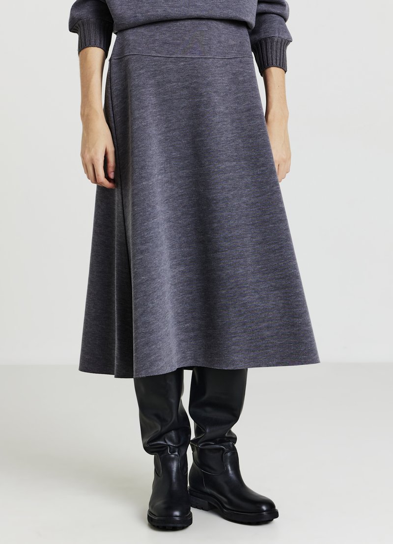 Grauer knie-langer Rock aus weichem Stoff mit glatter Textur, ausgestattet mit einem taillierten Bund und ausgestellter Silhouette, kombiniert mit schwarzen Stiefeln.