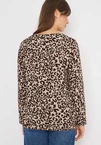 Top de manga larga con estampado de leopardo marrón y escote redondo, con un corte relajado y textura suave, combinado con pantalones de mezclilla azules.