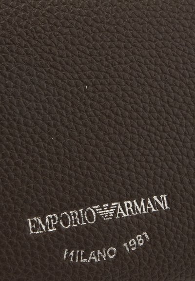 Черен текстуриран кожен повърхност с сребристо ембосирано лого Emporio Armani и текст "Milano 1981" в долния десен ъгъл.