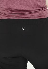 Svarta sportleggings med en slät yta, med elastisk midja och en liten vit 'Q'-logotyp på baksidan.