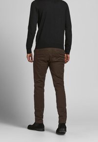 Maglione nero e chinos marroni indossati con scarpe in suede nere, mostrando la vista posteriore, con tasche piatte e un design aderente.