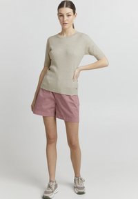 Top in maglia a coste beige con maniche corte abbinato a pantaloni corti in cotone rosa chiaro. Sneakers chiare con accenti grigi misti.