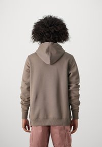 Hoodie in taupe, met een zachte textuur, geribde manchetten en zoom, en een relaxed fit. De achterkant toont een eenvoudig ontwerp.