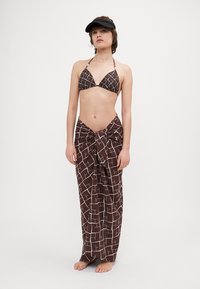 Bikini-top i brun og hvid ternet mønster, parret med en brun indpakningsskørt i lignende design, afsluttet med en bundet knude.