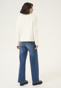 Un pull blanc duveteux associé à un jean bleu à jambes larges et des bottes noires chunky. Le pull a une coupe décontractée avec une texture douce.