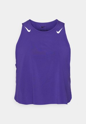 Violets bezsvītru sporta tops, izgatavots no viegla auduma. Tam ir balti Nike swoosh logotipi uz pleciem un apaļš kakla izgriezums.