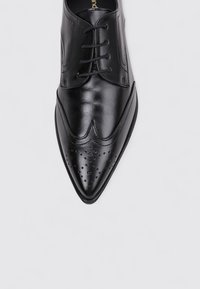 Zapato de vestir de cuero negro con punta afilada, superficie lisa y detalles perforados en la puntera. Presenta un diseño clásico con cordones.