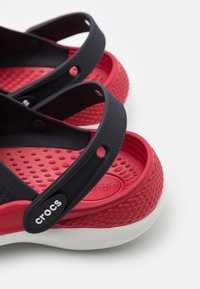 Czarno-czerwone sandały z teksturowanym wnętrzem, białą podeszwą i regulowanymi paskami. Logo "Crocs" z boku.