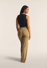 Top nero senza maniche e pantaloni larghi verde oliva a vita alta. Tessuto liscio con vita aderente e vestibilità rilassata lungo le gambe.