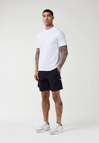 Biele tričko s krátkym rukávom a okrúhlym výstrihom, doplnené tmavomodrými cargo šortkami s bočnými vreckami a bielymi športovými teniskami.