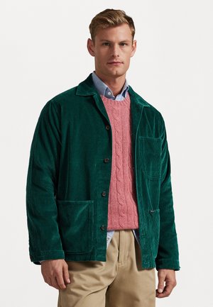 Green corduroy jacket with a relaxed fit, button closure, and a chest pocket, layered over a pink cable-knit sweater and a light blue shirt.