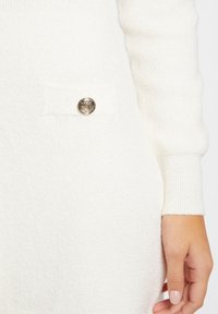 Abito bianco peloso con finitura testurizzata, tasca laterale con un bottone metallico decorativo e polsi a coste.
