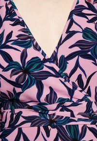 Robe portefeuille florale en tissu rose avec des motifs de feuilles bleues et vert foncé, avec un décolleté en V et un détail de surface texturé.