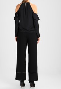 Haut noir à épaules nues avec des manches à volants et un dos en trou de serrure, associé à un pantalon noir à jambes larges avec des accents de couture blanche.