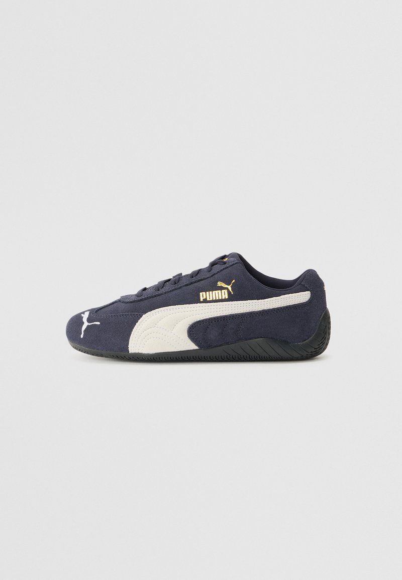 Încălțăminte sport din suede, de culoare bleumarin, cu bandă laterală albă și logo auriu, vârf rotund, talpă plată din cauciuc negru și accente texturate.