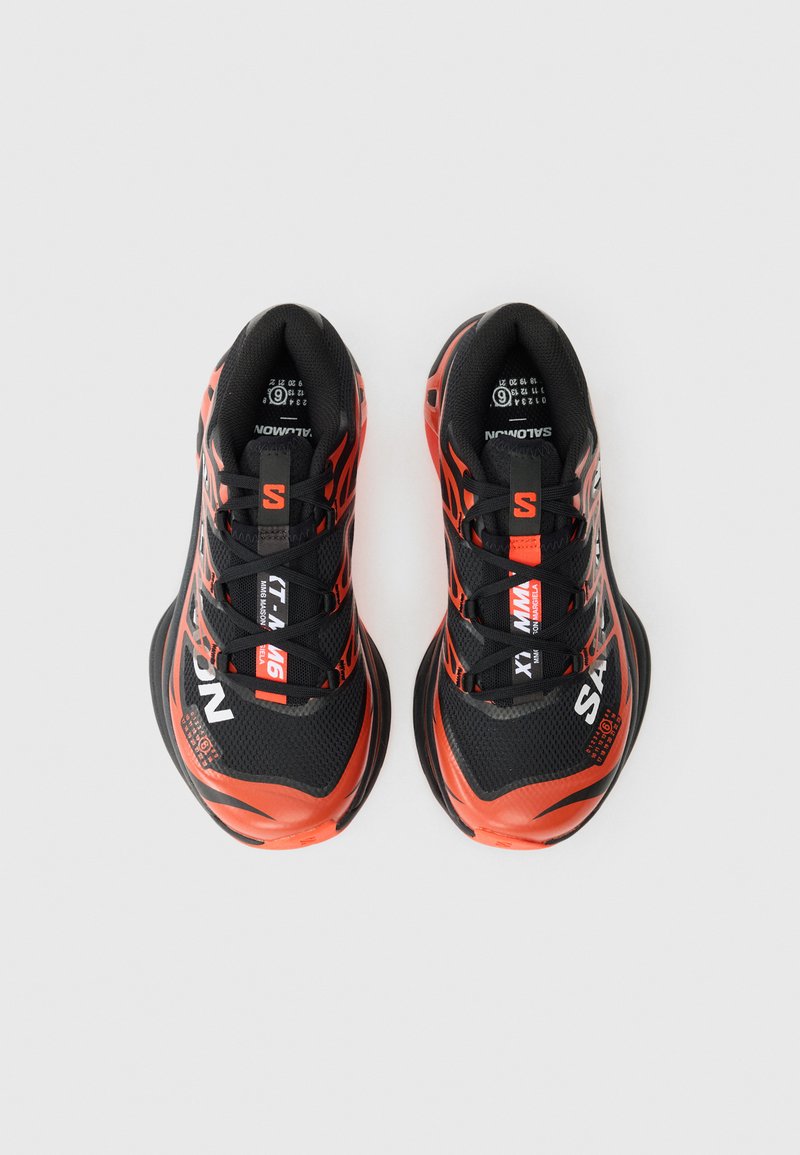 Baskets de sport rouges et noires avec tige en mesh, accents texturés et lacets noirs. Présente un logo en blanc, avec un design aérodynamique.