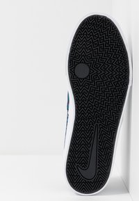 Černá gumová podrážka boty se vzorem ve tvaru cik-cak, bílými okraji a hladkým středovým kruhem. Barevné designové prvky podél strany.