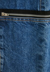 Tejido de mezclilla azul con cierre visible y ribete negro. Incluye costuras en contraste y un patrón de superficie texturizada.