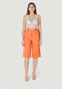 Culotte arancioni in lino con vita a cintura e gambe larghe, abbinati a un reggiseno in pizzo bianco con bordi scallop e scollatura profonda.