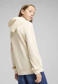 Felpa beige con cappuccio e vestibilità rilassata, caratterizzata da maniche lunghe e polsini a costine, abbinata a una gonna di jeans. Tessuto dalla superficie liscia.