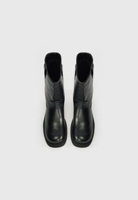 Bocanci din piele neagră, cu un finisaj neted, margini superioare curvate și tălpi plate din cauciuc. Include bucle laterale pentru a facilita îmbrăcarea.