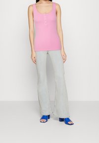 Rosa ribbad linne med rundad halsringning och detalj med fem knappar, parat med ljusblå utsvängda jeans och blå öppna klackskor.