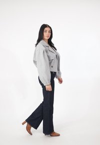 Grå croppet jakke med oversized pufærmer og dobbeltradet design, kombineret med mørke, udvidede jeans og brune støvler med hæl.