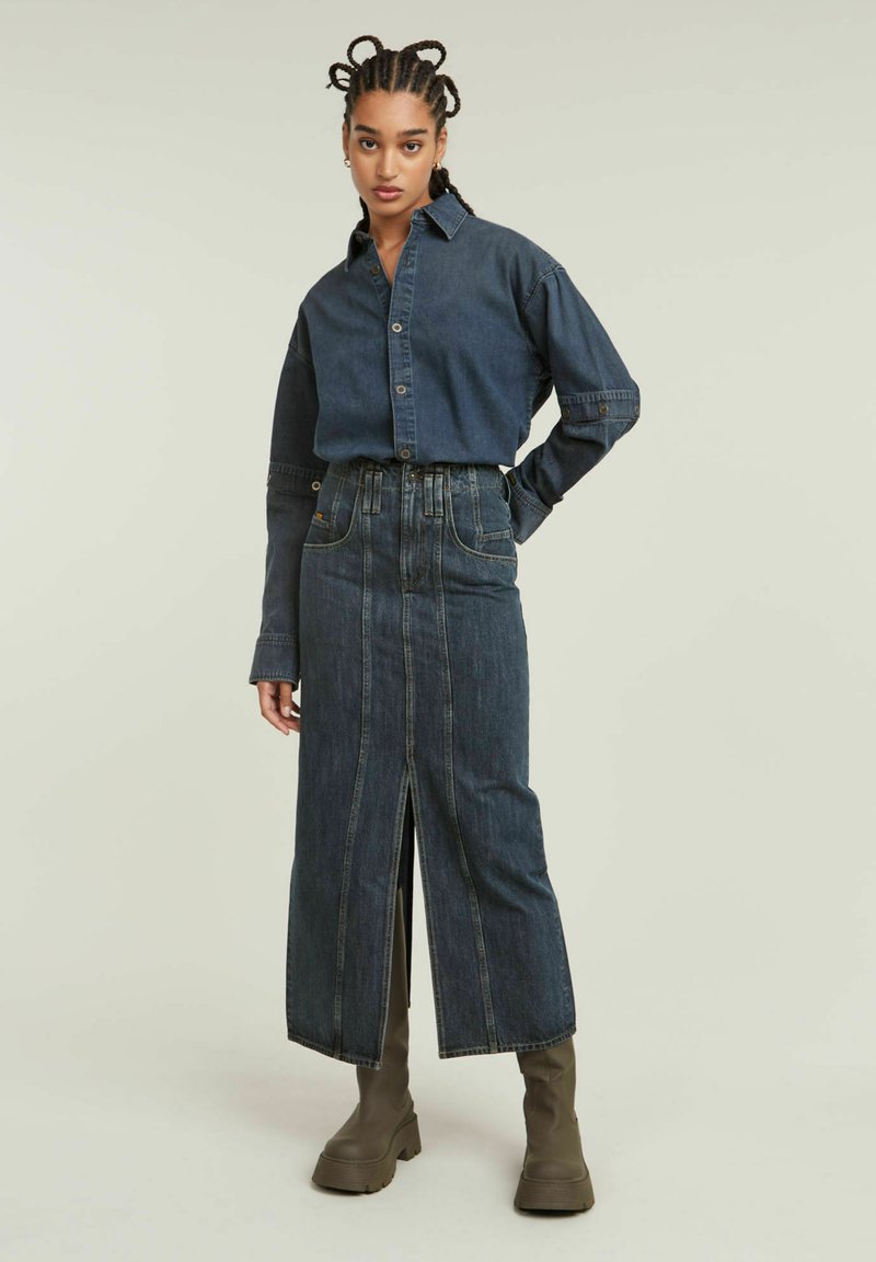 Jeanshemd mit Knopfverschluss, langen Ärmeln und dunkler Waschung. Der hochgeschnittene Rock hat einen Schlitz vorne und kontrastierende Nähte.