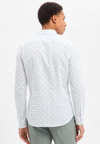 Camicia a maniche lunghe con bottoni, bianca con un motivo di foglie verde chiaro. Presenta un colletto stretto, orlo curvo e silhouette aderente.