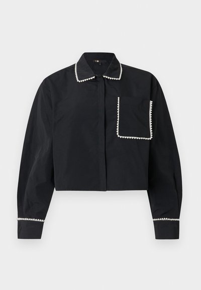 Μαύρο μακρυμάνικο κοντό μπλουζάκι με τσέπη μπροστά, γιακά και μανσέτες διακοσμημένες με λευκές χάντρες που μοιάζουν με πέρλες.