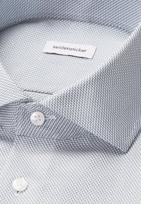 Col de chemise à motifs bleus avec une texture en chevrons, comportant une étiquette blanche et des accents de boutons, affichant un design moderne.