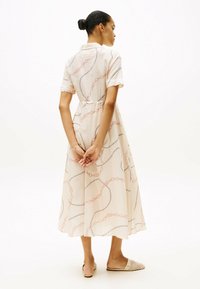 Lysebeige kjole med kædelinkmønster i pink og sort, korte ærmer, knappet krave, indsnævret talje og flydende nederdel.