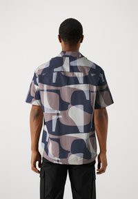 Lyhythihainen paita, jossa on geometrinen kuosi, navy, mauve ja vaaleanharmaat sävyt. Valmistettu sileästä kankaasta, rento malli ja kaulus.