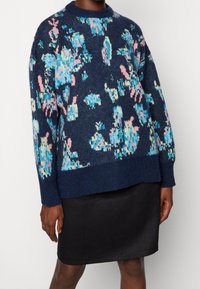 Pull-over en tricot bleu foncé avec un motif floral en turquoise et rose. Comprend un col rond et une coupe décontractée.