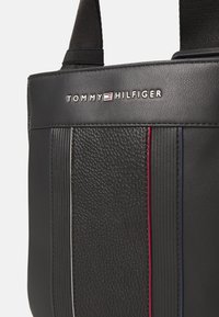 Black synthetic tote bag with textured front, featuring vertical ridges and red, white, and blue accents. Silver logo prominently displayed.