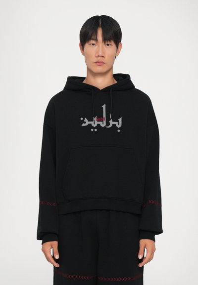 Felpa nera con cappuccio e tasca a marsupio, caratterizzata da una stampa grigia e rossa. Maniche lunghe con cuciture decorative rosse ai polsini.