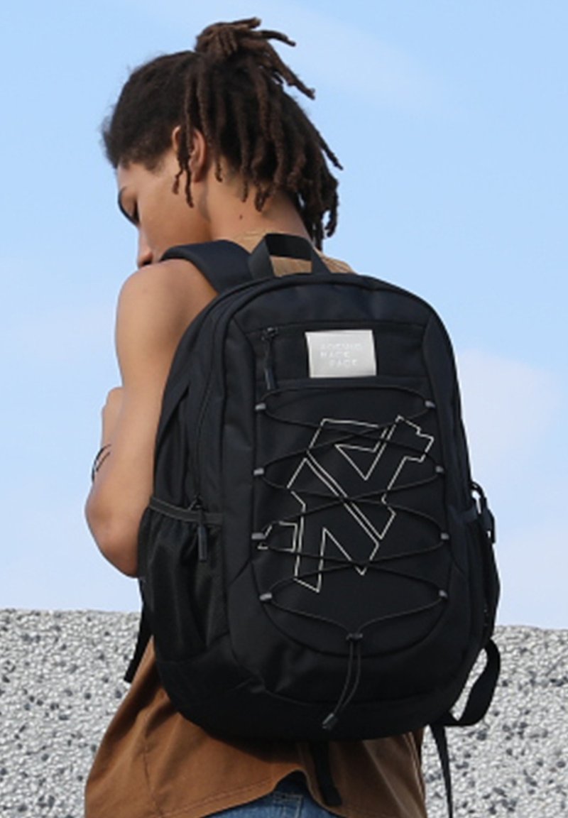 Zaino nero realizzato in tessuto resistente, con un design geometrico caratterizzato da dettagli elastici, tasche laterali e un piccolo scomparto anteriore con zip.