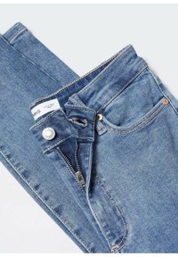 Jean en denim bleu avec fermeture éclair frontale partiellement ouverte, bouton en métal et poche avant visible, posé à plat sur un fond blanc.