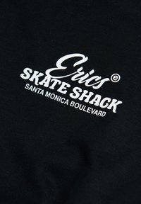Tela negra con texto blanco que dice "Eris Skate Shack Santa Monica Boulevard" en tipografías mixtas y en negrita.