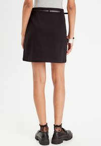 Jupe noire à la silhouette droite, avec des passants de ceinture et une taille. Portée avec des chaussures noires et des chaussettes en mesh à motifs de cœurs.